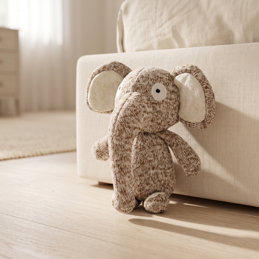 Nino knit dog toy on a pale oak floor beside a cream linen bed base in soft morning light