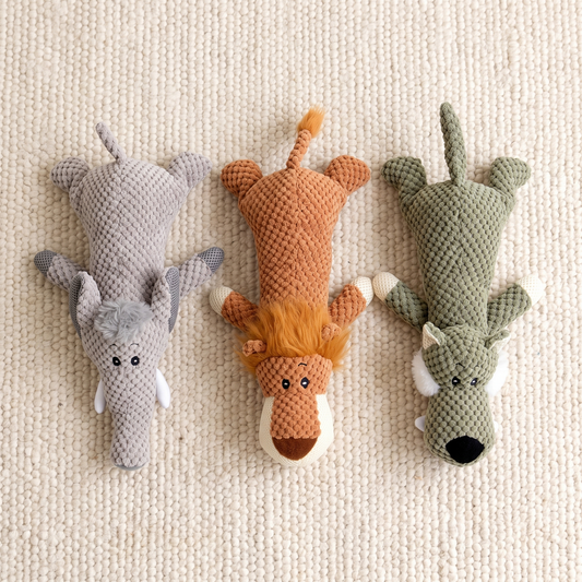 Selva flat dog toys in grey, rust and sage laid out on a cream wool rug, seen from above