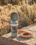 Load image into Gallery viewer, Arno Travel Bottle on a sunlit stone step beside a tan leather leash
