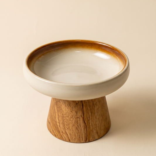 Cima Elevated Bowl — cream glazed ceramic basin with a reactive amber rim on a turned solid wood pedestal
